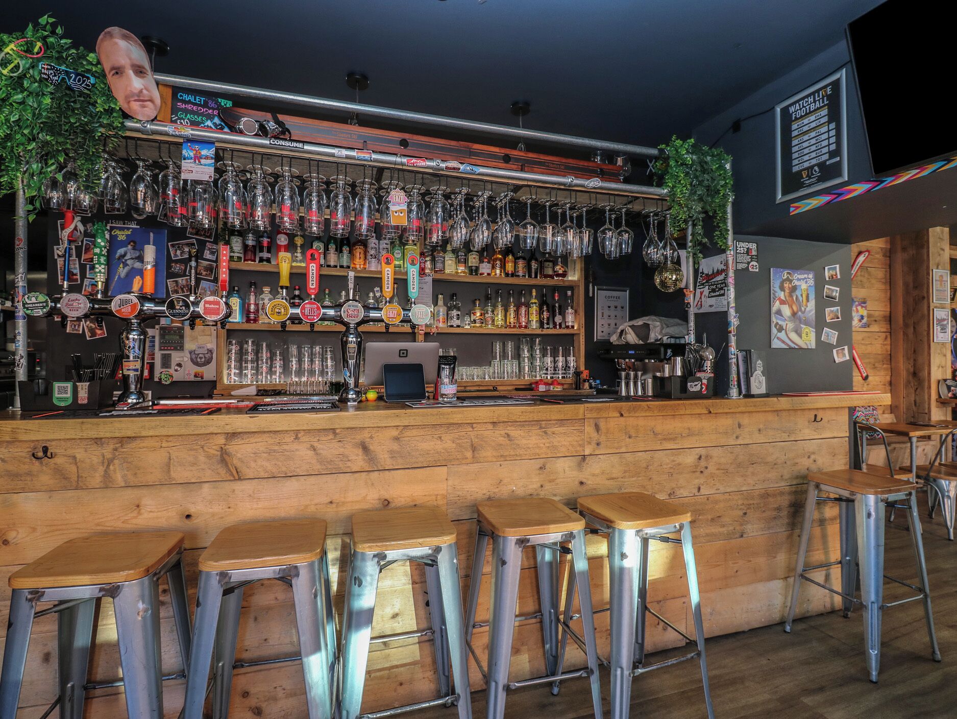 A bar with a wooden counter, metal stools, and a variety of bottles and glasses.