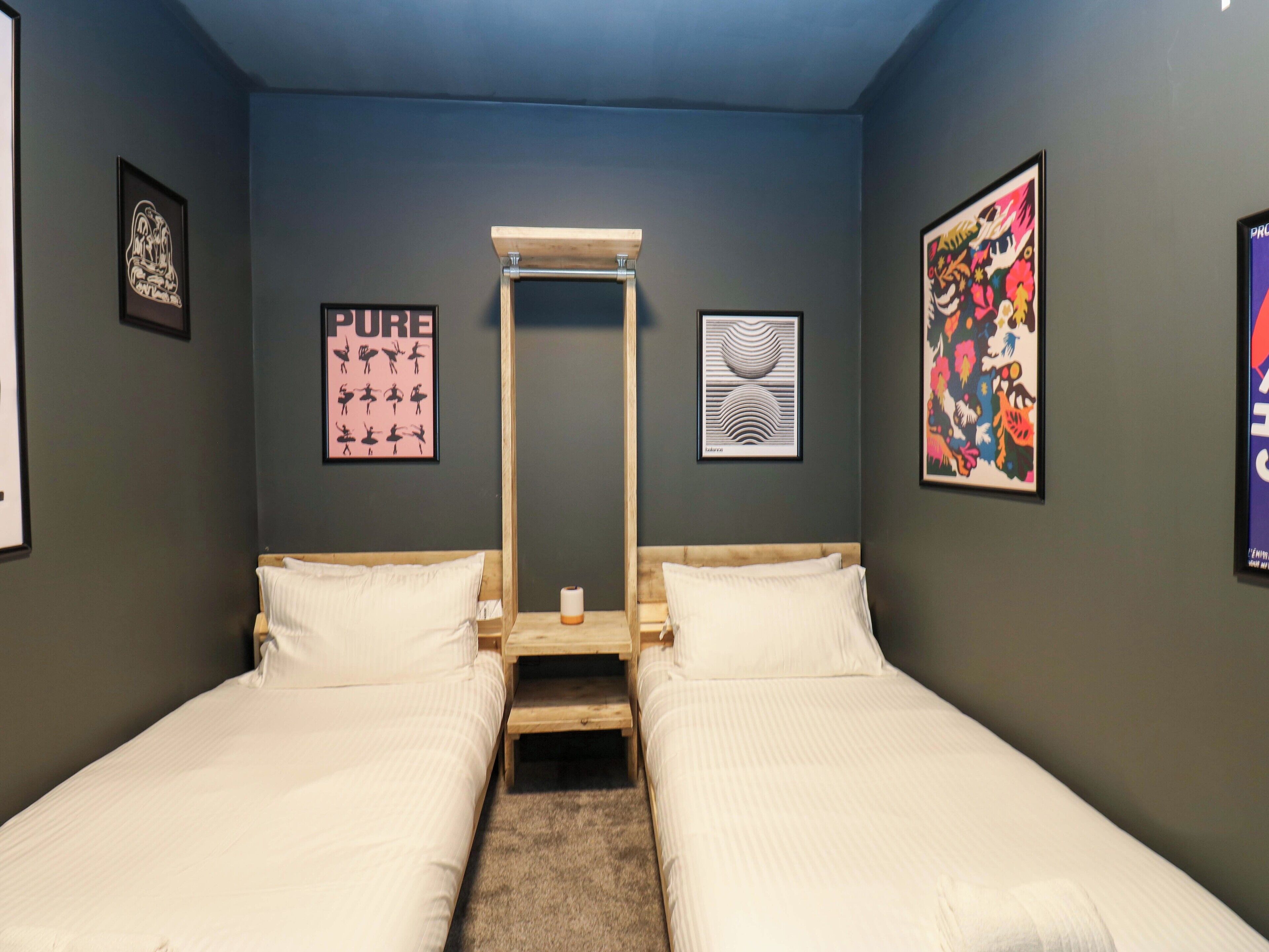 Une chambre avec deux lits, une échelle en bois et des œuvres d’art accrochées aux murs.