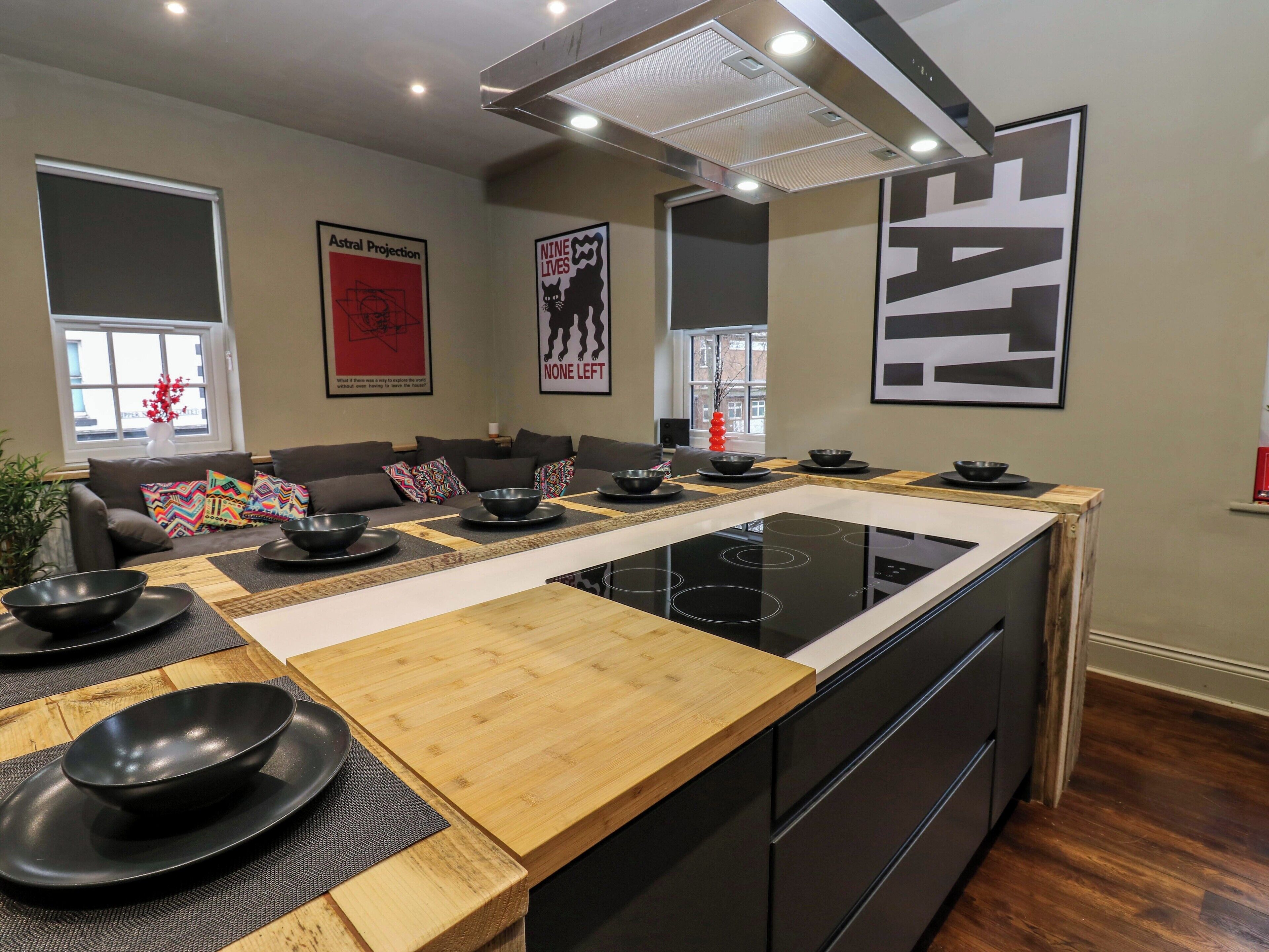 A modern kitchen with an island, black appliances, and a dining area with a sofa and colorful cushions.