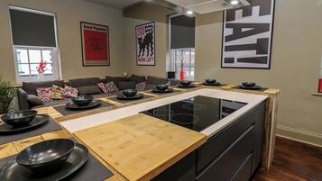 A modern kitchen with an island, black appliances, and a dining area with a sofa and colorful cushions.
