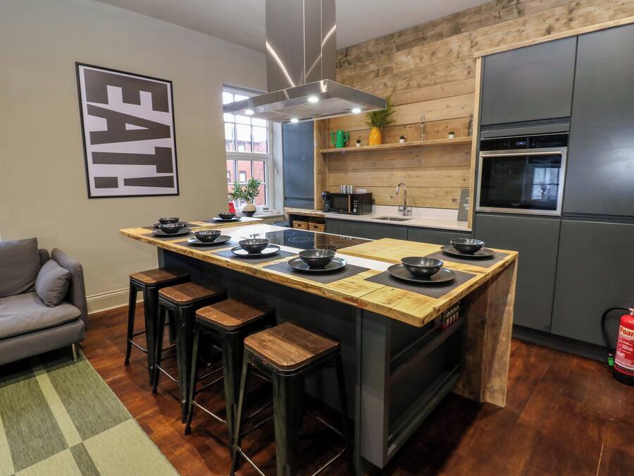 Una cocina moderna con una isla central, taburetes de bar, horno empotrado y una pared de madera.