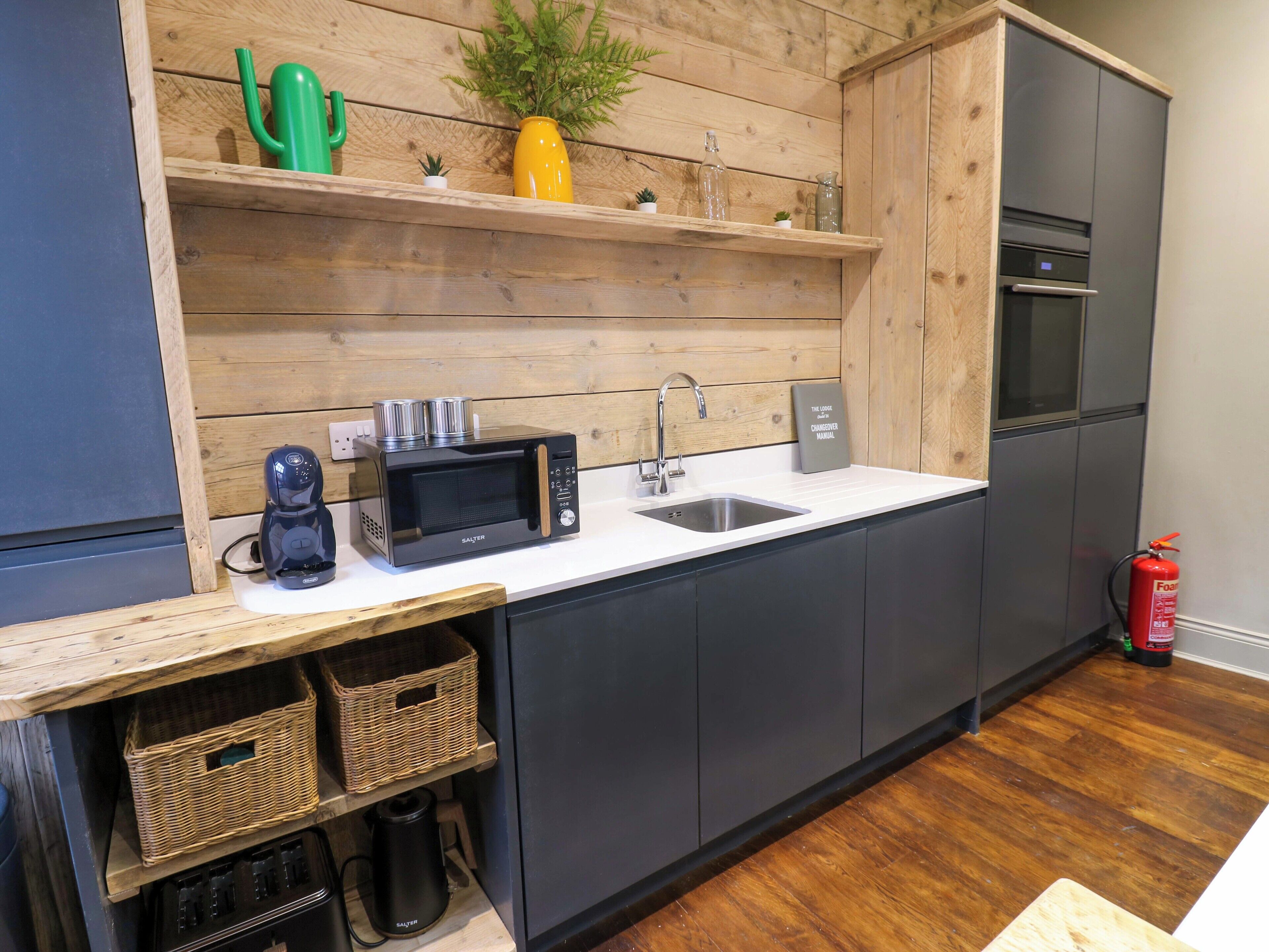 A modern kitchen with a built-in microwave, a coffee maker, and a sink. There are wooden shelves above the counter with decorative items.