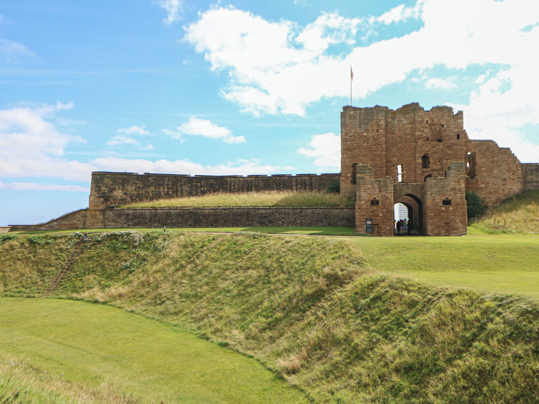 A historic stone castle ruin with a large arched entrance, surrounded by grassy fields and a clear sky.