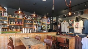 Eine Bar mit Holzkabinen, einer Theke voller Flaschen und einem Kleiderständer mit lässiger Kleidung.