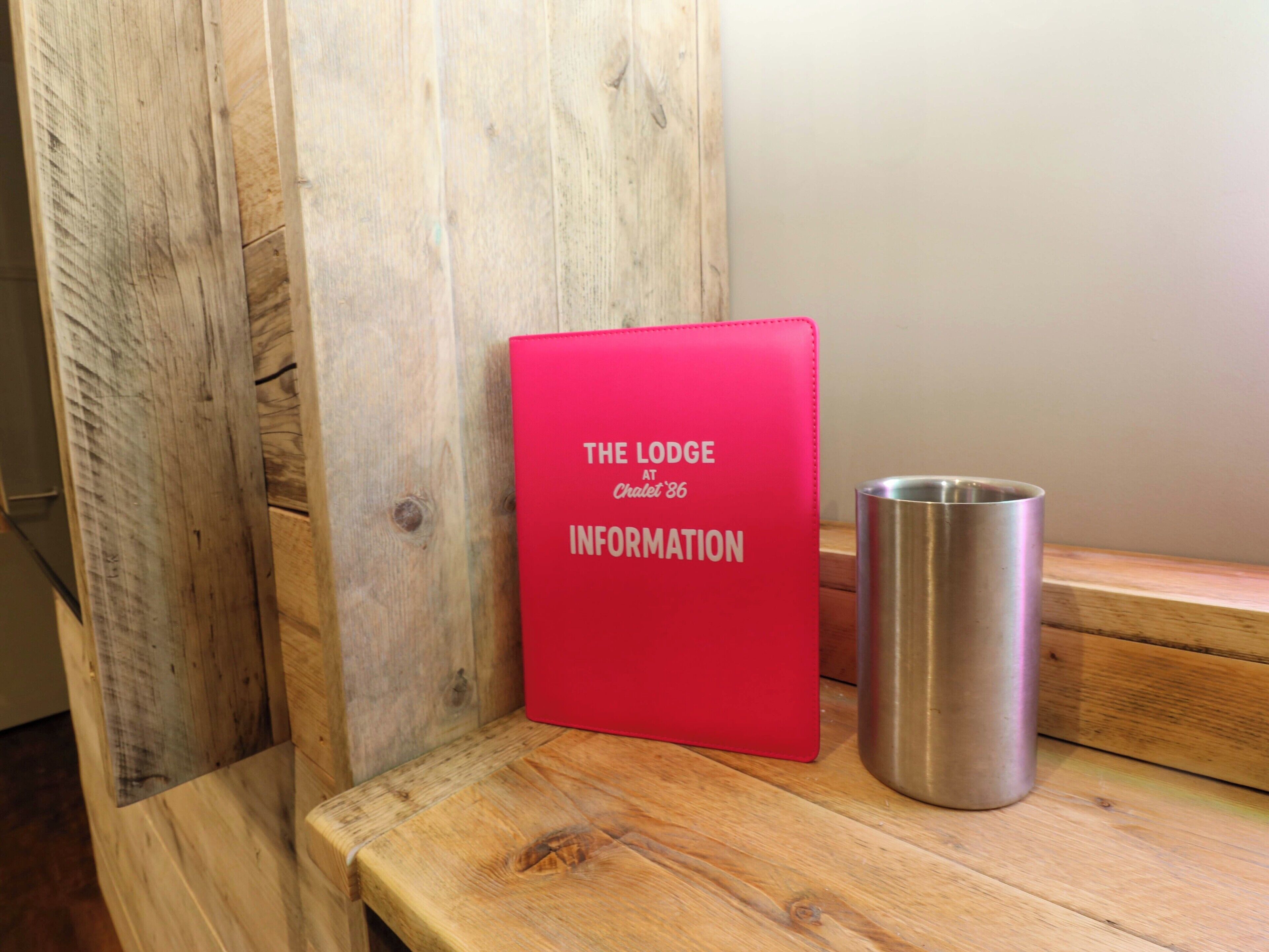A red folder labeled "The Lodge at Chalet 86 Information" on a wooden bench.