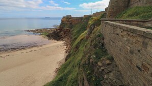 Blick auf die Küste mit einem Sandstrand und einer Steinmauer.