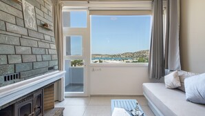A balcony with a stone fireplace, a sofa, and a view of a coastal landscape. - Holiday Home 'Saphhire' with Sea View, Shared Terrace and Wi-Fi (Paros)