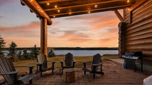 A log cabin with a patio, outdoor seating, a grill, and a view of a lake at sunset. - Stone Skipper | Waterfront! Private Dock! Boat Ramp! Hot Tub! (Island Park)