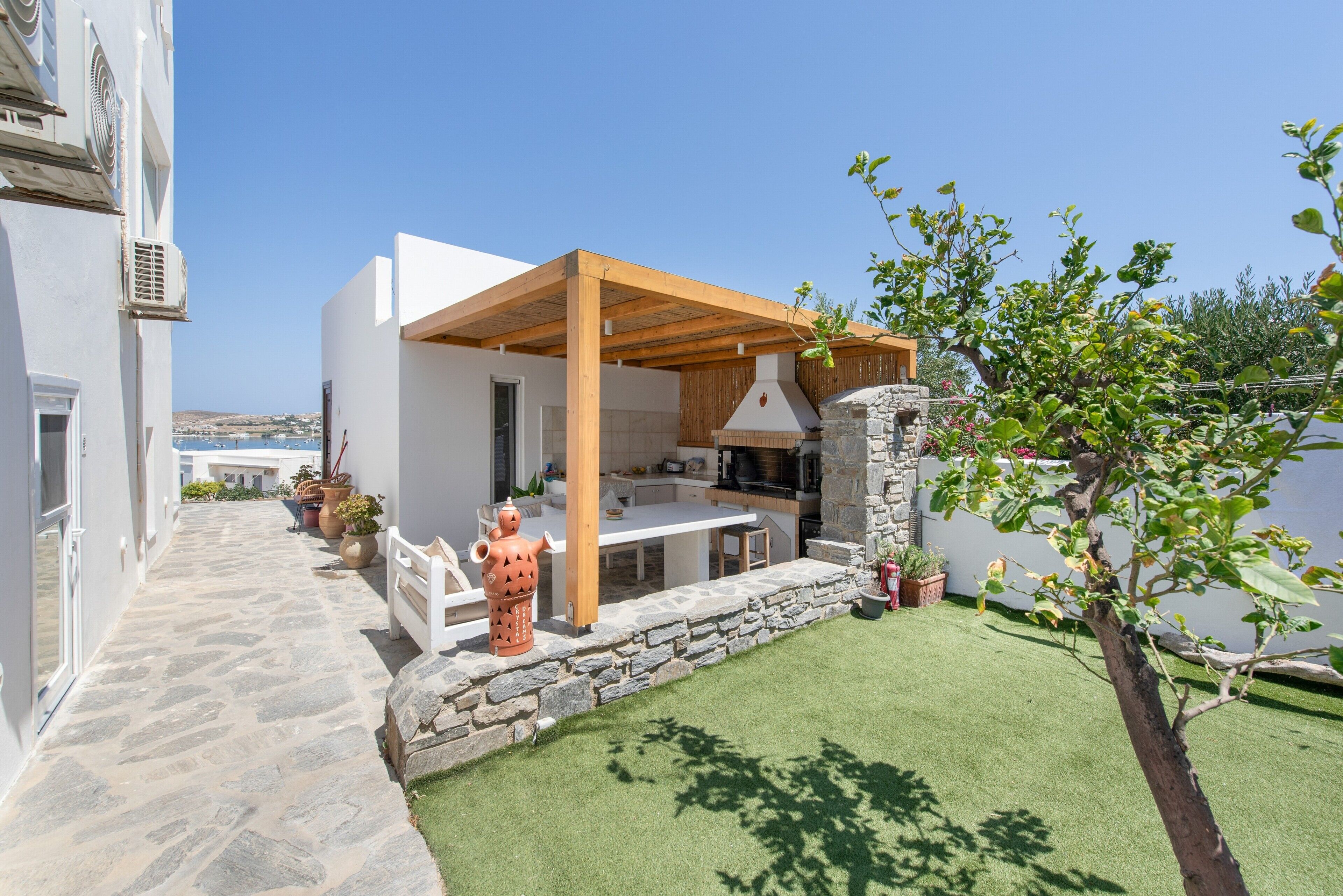 Un área de cocina al aire libre moderna con paredes de piedra, una pérgola de madera y vistas al mar.