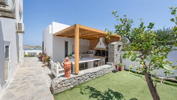 Un área de cocina al aire libre moderna con paredes de piedra, una pérgola de madera y vistas al mar.