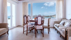 A room with a dining table, four chairs, a sofa, and a view of the sea. - Diamondbig House Country Home with Jacuzzi and Wi-Fi (Paros)