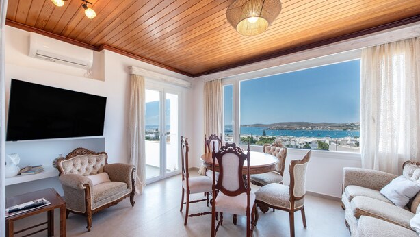 A spacious living room with a wooden ceiling, a flat-screen TV mounted on the wall, a round dining table with chairs, and a sofa. - Diamondbig House Country Home with Jacuzzi and Wi-Fi (Paros)