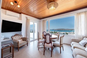 A spacious living room with a wooden ceiling, a flat-screen TV mounted on the wall, a round dining table with chairs, and a sofa. - Diamondbig House Country Home with Jacuzzi and Wi-Fi (Paros)