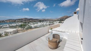 A balcony with a wicker chair and table, overlooking a coastal town and mountains. - Diamondbig House Country Home with Jacuzzi and Wi-Fi (Paros)