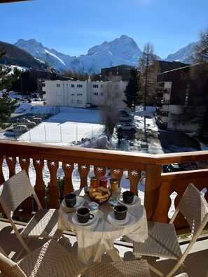 A balcony with wicker chairs and a table set for breakfast, overlooking a snowy mountain landscape and a building with multiple windows. - Studio 'Charmant au pied du Jandri' with Mountain View and Balcony (Les Deux Alpes)