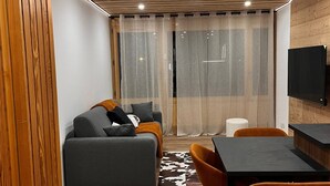 Una sala de estar moderna con un sofá, mesa de comedor, sillas y un televisor montado en la pared.