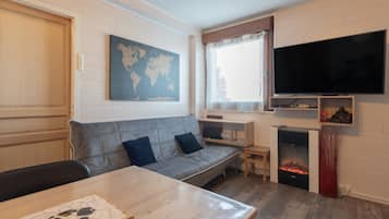 Una sala de estar acogedora con un sofá gris, una mesa de madera, un televisor de pantalla plana, una chimenea y un mapa del mundo en la pared.