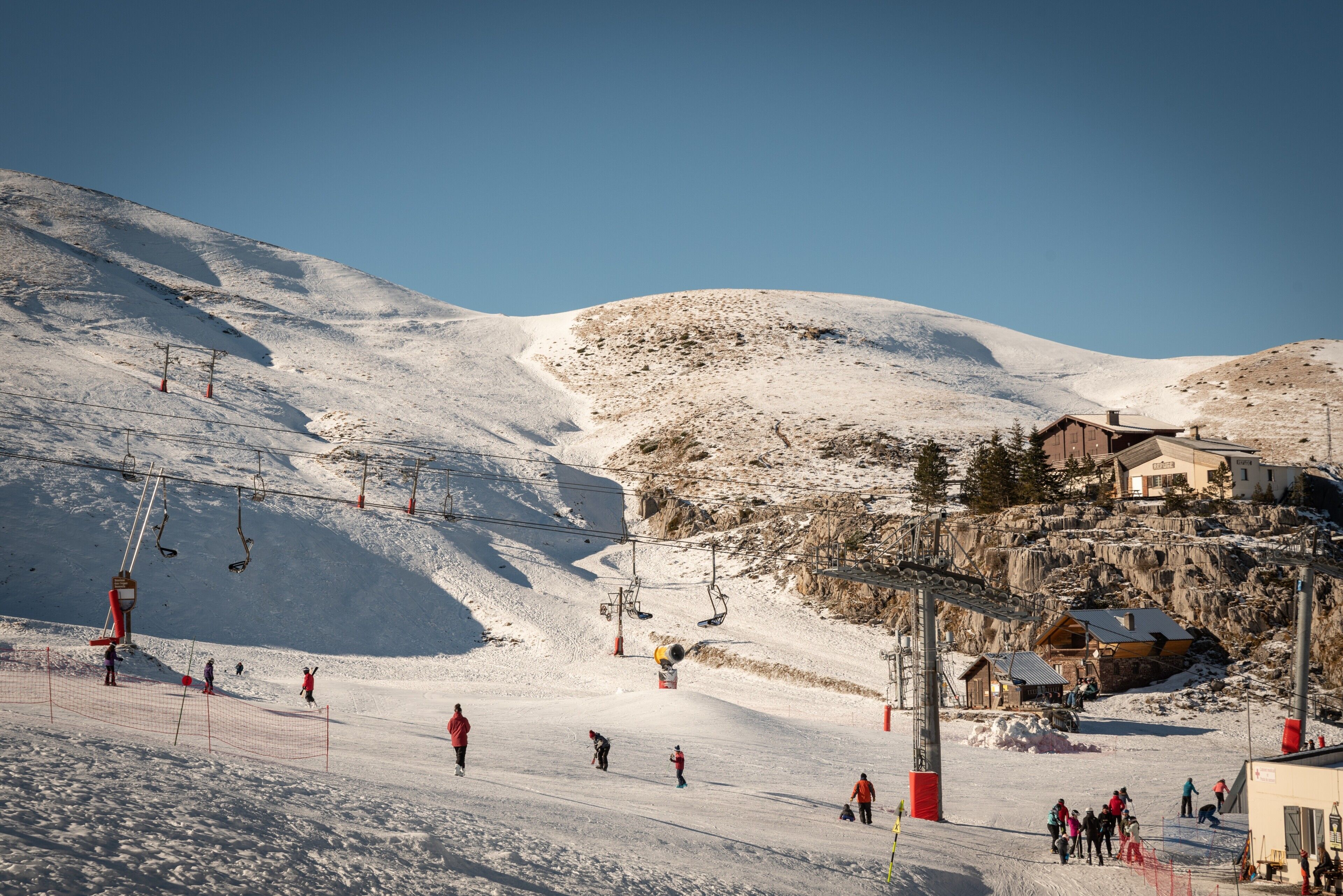 Une station de ski dotée d’un télésiège, de pistes enneigées et d’un bâtiment au toit en pente.