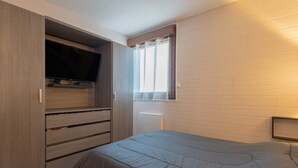 Un dormitorio con cama, armario, televisor y ventana con cortinas.
