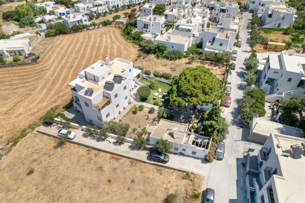 An aerial view of a residential area with modern white buildings, a green space with trees, and a clear road. - Citrine Studio with Balcony, Sea & Mountain View, Wi-Fi (Paros)