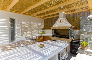 Una cucina esterna moderna con parete in pietra, soffitto in legno e barbecue integrato.
