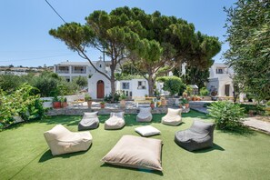 A courtyard with outdoor seating, a white building with a cross, and trees. - Holiday Home 'Amethyst Romantic Apartment With' with Sea View, Shared Terrace and Wi-Fi (Paros)