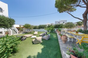 A courtyard with artificial grass, outdoor seating, and potted plants. - Holiday Home 'Amethyst Romantic Apartment With' with Sea View, Shared Terrace and Wi-Fi (Paros)