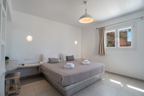 A bedroom with a bed, bedside table, lamp, and a window with curtains. - Holiday Home 'Amethyst Romantic Apartment With' with Sea View, Shared Terrace and Wi-Fi (Paros)