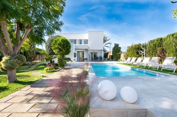 A modern house with a swimming pool, surrounded by well-maintained lawns and trees.