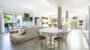 Ein modernes Wohnzimmer mit einer Couch, Sesseln, einem runden Tisch und einer Küchenzeile mit Schränken und einem Herd.
