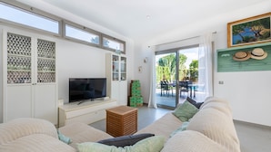 Ein modernes Wohnzimmer mit einem Flachbildfernseher, einer Couch, einem kleinen Holzschemel und einer Glastür zum Essbereich im Freien.