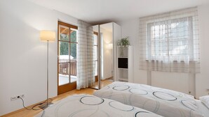 Ein Schlafzimmer mit zwei Betten, einem Nachttisch, einer Lampe, einem Fernseher und Blick ins Freie.
