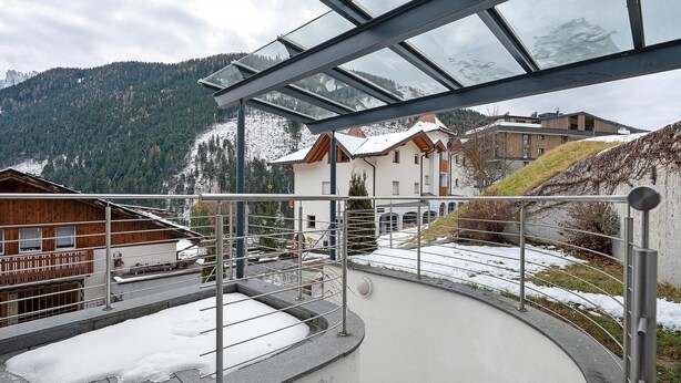 Ein modernes Gebäude mit Glasdach, verschneitem Untergrund und Blick auf eine gebirgige Landschaft.