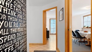 Ein Flur mit einer Wand mit motivierenden Sprüchen, eine Holztür, die zu einem Essbereich mit Tisch und Stühlen führt.