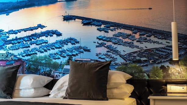 A bed with pillows and a view of a marina with boats. - Hotiday Napoli Lungomare (Naples)