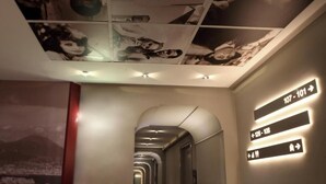 A hotel corridor with directional signs and a ceiling with framed photos. - Hotiday Napoli Lungomare (Naples)