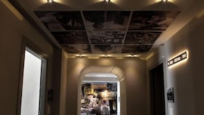 A hallway with a ceiling decorated with various photographs and a sign indicating room numbers. - Hotiday Napoli Lungomare (Naples)