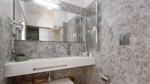 A bathroom with a white vanity, a large mirror, a towel rack, and a towel shelf. - Hotiday Napoli Lungomare (Naples)