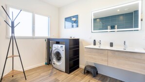 Ein modernes Badezimmer mit Waschmaschine, großem Spiegel und Holzboden.