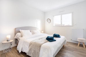 Un dormitorio con cama, mesita de noche, lámpara y ventana.