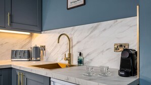 Een moderne keuken met een marmeren aanrechtblad, een gouden kraan, een koffiezetapparaat en een vaatwasser.