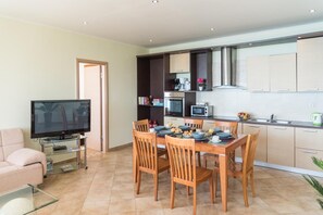 A modern living room with a flat-screen TV, a glass coffee table, a sofa, and a dining area with wooden chairs and a table set for breakfast. - Villa 'Belle Plaza' with Sea View, Wi-Fi and Air Conditioning (Γαρδενος)