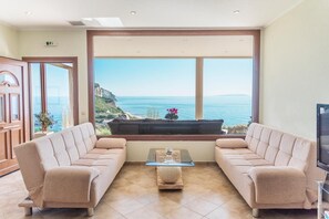 A room with a large window offering a view of the sea, two sofas, a small table, and a television. - Villa 'Belle Plaza' with Sea View, Wi-Fi and Air Conditioning (Γαρδενος)