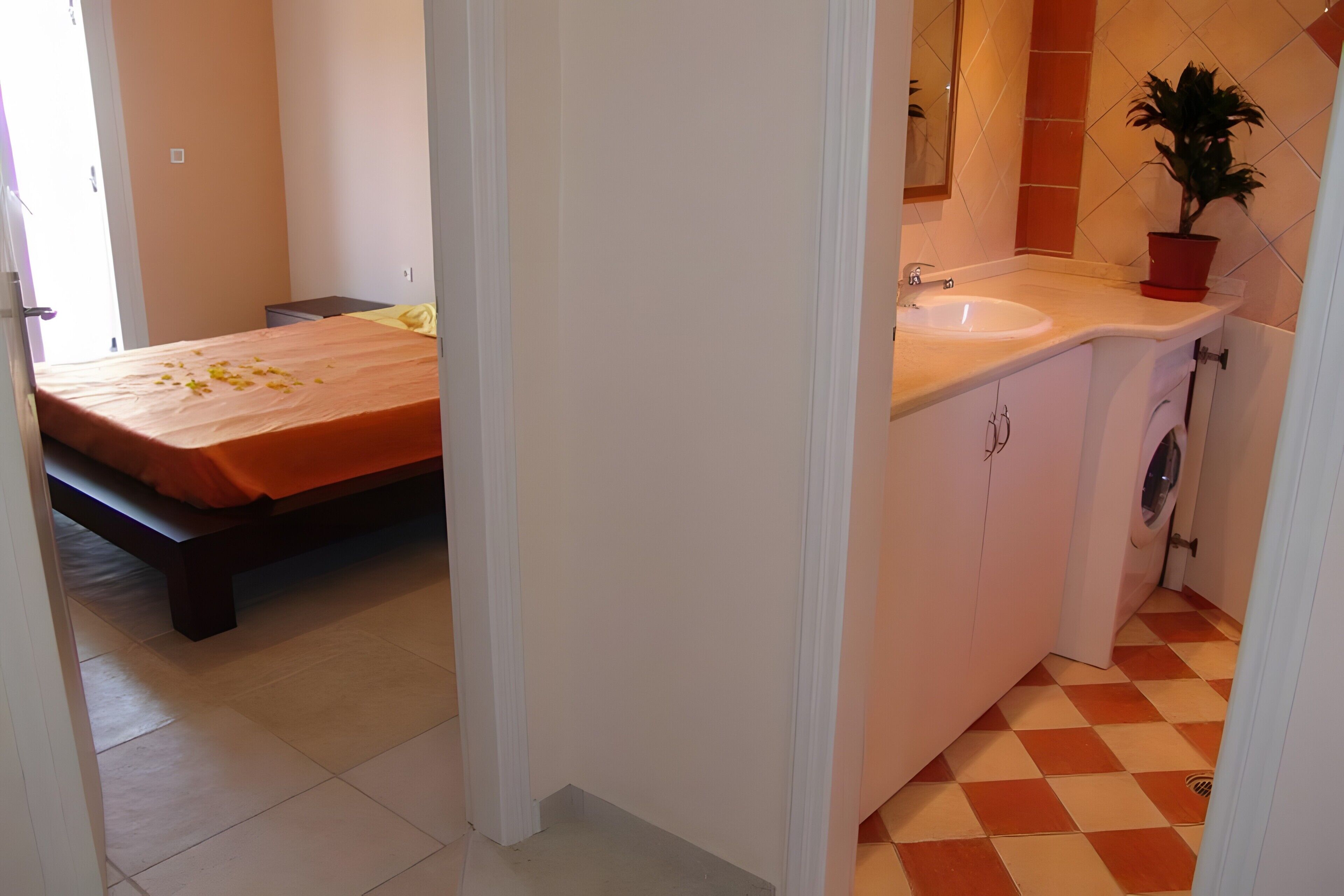 Un dormitorio con cama, un baño con lavamanos y una planta en maceta, y suelo a cuadros.