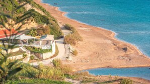 A coastal landscape with a beach, cliffs, and a building with a red roof.