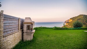 A stone wall, a small structure, and a grassy area with a view of the sea and a hill.