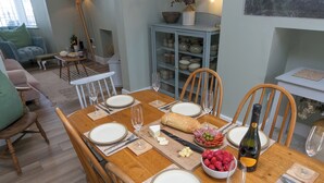 Comedor con una mesa de madera dispuesta para seis personas, con platos, cubiertos y una botella de vino.