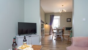 Una sala de estar con televisor, una mesa de comedor con sillas y un sofá rosa.