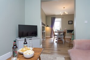 A living room with a TV, a dining table with chairs, and a pink sofa. - Modernised home 5 minutes from Newborough Beach - Pas the Keys (Wales)