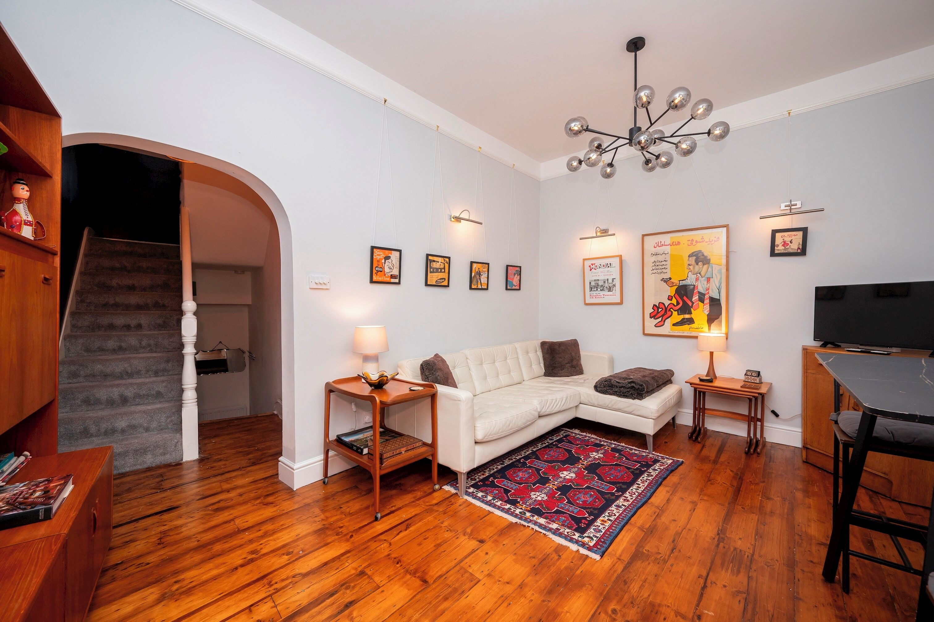 A living room with a sofa, a coffee table, a TV, a staircase, and a chandelier.